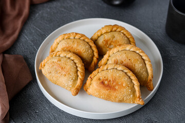 Top view arrangement of golden brown Pastel, a savory deep-fried pastry with beautifully crimped edges, on a clean white plate. A popular snack or appetizer. 