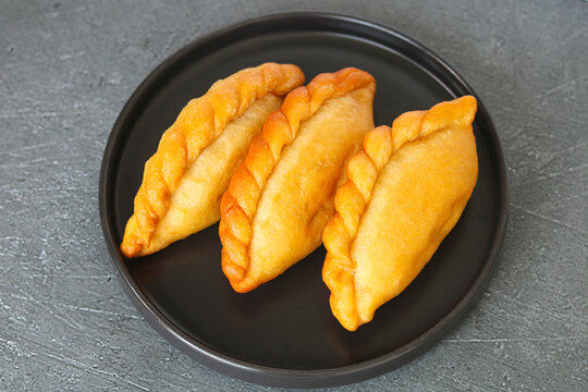Three golden-brown Panada pastries arranged on a dark plate.