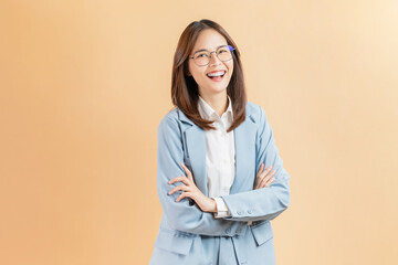 Smiling Asian businesswoman standing with arms crossed isolated against a beige background.