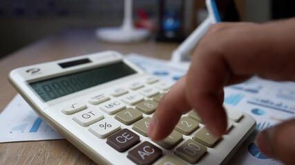 Close-up of a hand pressing buttons on a calculator with financial documents in the background - Powered by Adobe