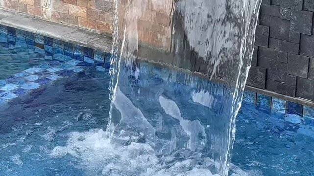 Water cascading down from wall feature into blue swimming pool.