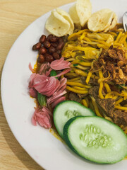 A plate of traditional Indonesian Mie Aceh served with rich spicy curry sauce, beef, cucumber slices, peanuts, crackers, and fried shallots on top.