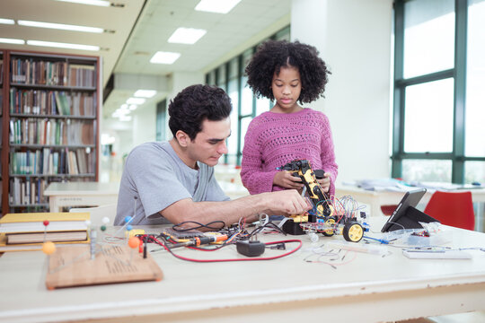 A teacher guiding students in a robotics project during a STEM class in the library