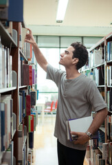 A young man stands between the shelves of a library © Wosunan