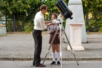 Outdoors, teacher explains the use of a telescope component to a student standing beside the mounted instrument, highlighting hands-on learning and practical astronomy guidance