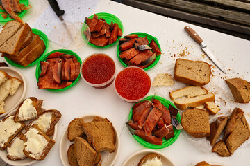 Traditional meal with bread, salmon, and red caviar. A rustic spread of bread, smoked salmon, and bowls of red caviar is served on a white table, representing traditional coastal cuisine 