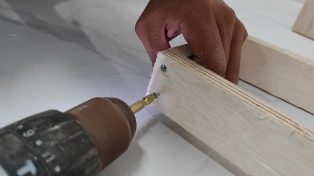 Close-up of a worker’s hand using an electric drill to drive a screw into a wooden board. This image highlights DIY woodworking, carpentry craftsmanship, construction work, and home improvement projec - Powered by Adobe