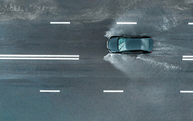 car is driving fast with spray on a flooded road after a downpour. aerial top view from flying...