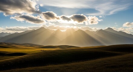 Sun rays breaking through clouds over mountain range and grassy hills