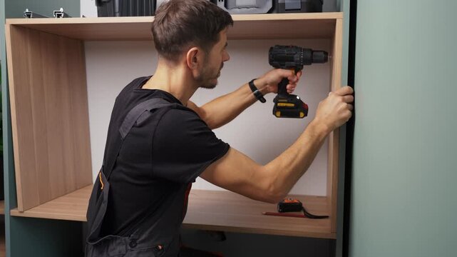 Man drilling hole in side panel of wooden cabinet with electric drill. Home furniture assembly during renovation in apartment