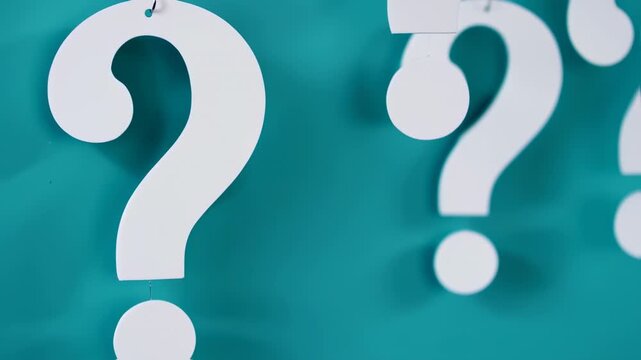 Close-up of white question marks suspended against a turquoise background