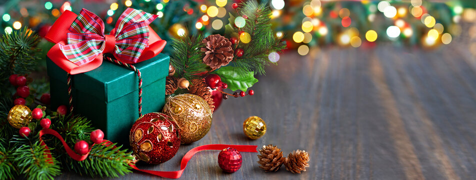 Christmas Green gift box with plaid ribbon, red and gold ornaments, and twinkling lights on a wood surface.