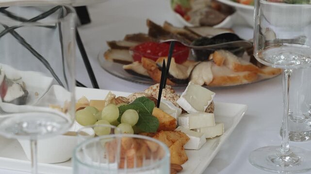 Caucasian woman hands stick skewers into appetizers on table. Waiter serves cheese and fruit platter at banquet. Prepared food and tableware for dinner.