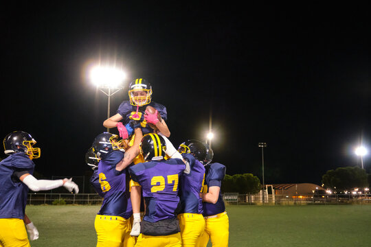 Football players lifting a teammate, celebrating success and teamwork under stadium lights