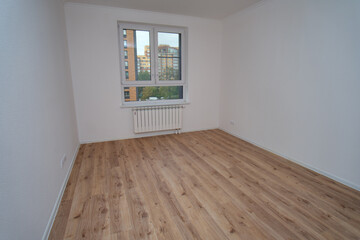 Wide shot of an empty apartment room with light wood laminate flooring and white walls. Renovated residential interior space design concept.