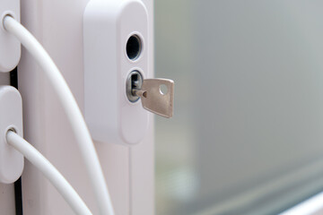 Small silver key inserted into a white lock on a home window. Safety and security concept for domestic and residential properties.