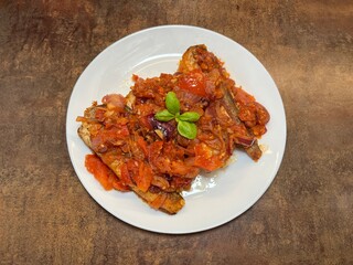 Fried fish topped with spicy tomato sauce and fresh herbs. Homemade comfort food served on a white plate, perfect for culinary photography