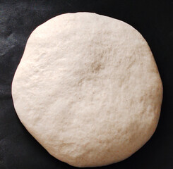 Round raw bread dough on a dark background.
