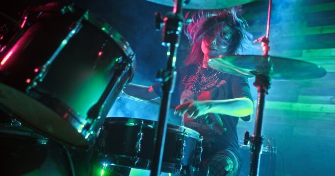 Female Musical artist performs on the stage of nightclub. Girl plays drums masterfully with drumsticks. The performance is accompanied by multi-colored light show