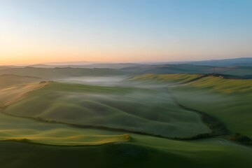 Golden sunrise illuminates rolling green hills and valleys shrouded in a gentle mist creating a serene and breathtaking natural landscape at dawn