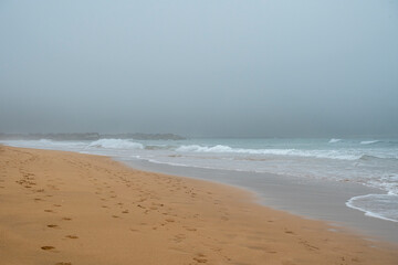 An empty beach with only footprints along the shore. The sky is cloudy, creating a serene atmosphere. The beach is deserted.