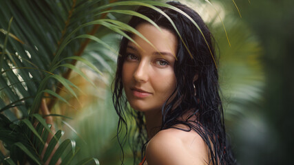 Fototapeta premium Elegant Woman in Orange Bikini, Wet Hair, Surrounded by Tropical Foliage