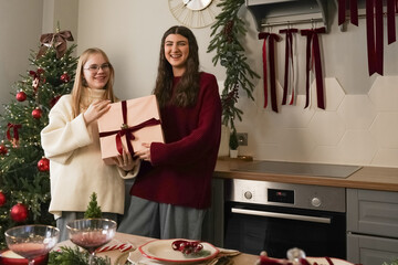Two friends celebrating Christmas in a cozy kitchen while sharing a gift together