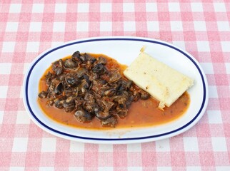 Plate of snails with tomato sauce on a rustic checkered tablecloth. It' is also called escargot.