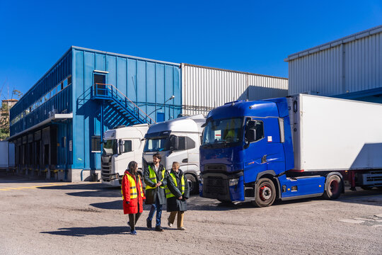 Logistics workers walking near transport trucks at cold storage warehouse