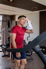 Asian middle aged healthy man wiping sweat with towel after running exercising on a treadmill in gym