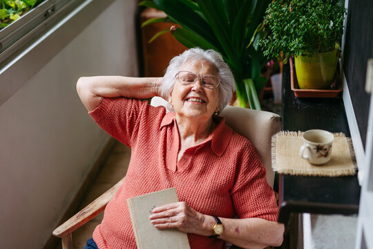 Old woman relaxing at home, sitting with book in chair, having closed eyes.