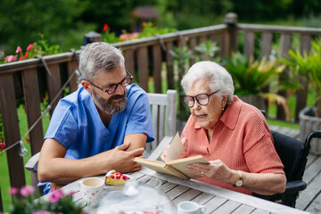 Caregiver spending time with elderly woman, reading book.