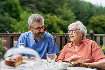 Caregiver spending time with elderly woman, reading book.