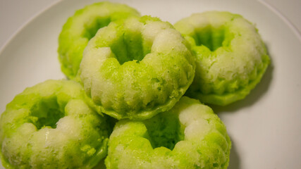Close-up of a traditional Indonesian cake called putu ayu, a sweet, fragrant cake topped with coconut—white background.