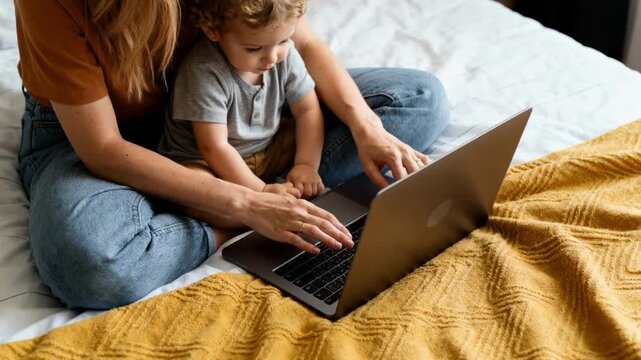 Parent and toddler using a laptop together on bed in cozy home setting, learning and bonding during remote work and online education time with family technology and support