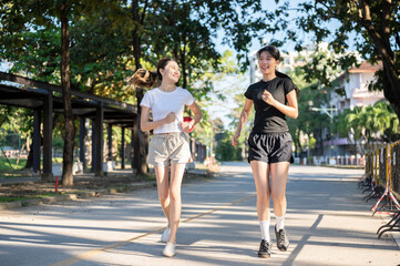 Obraz premium Pretty asian woman looking at friend while running or jogging on concrete road exercising in a park.