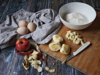 Flat lay of ingredients for apple pie on rustic wooden background. Peeled and chopped apples, flour, eggs, and kitchen knife on wooden board.