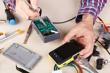 Master checks electrical components of device with compact oscilloscope at service workplace.