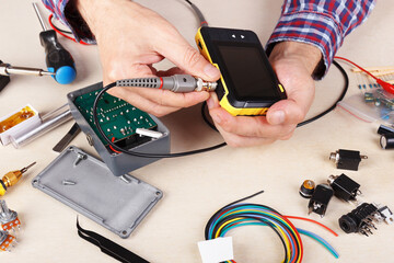 Serviceman checks electrical hardware with compact oscilloscope at service workplace.