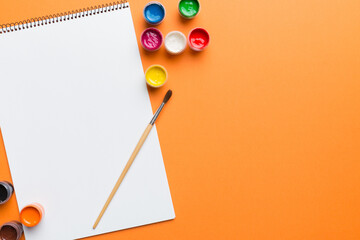 Album pages and paints, pencils, brush on a colored background. Top view with empty space. workplace for creativity. home teaching concept drawing