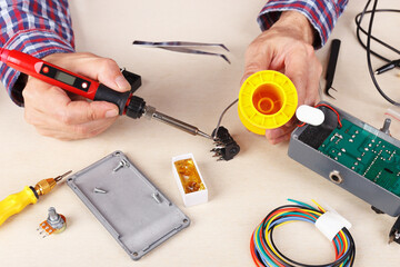 Repair electrical hardware with soldering iron at service workplace.