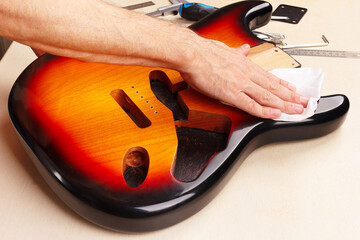 Guitar repairer wipes body of electric guitar.