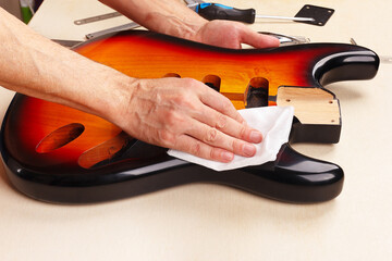 Guitar technician wipes body of electric guitar.