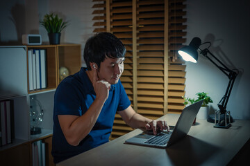 happy young man using wireless earbuds to listening music and laptop at night