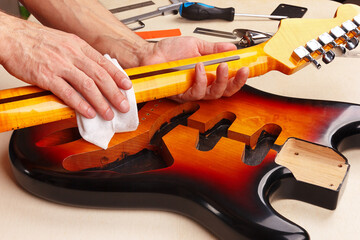 Guitar repairer polishes neck of electric guitar.