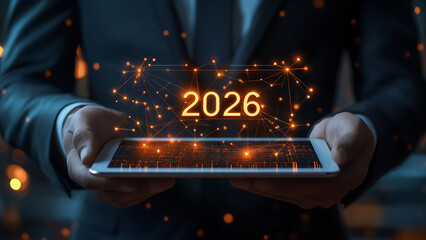 A man in a suit holds a tablet with "2026" written on it in bright orange. This image represents the theme of future-oriented technology.