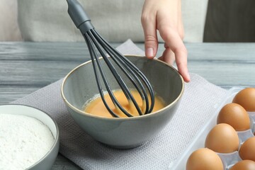 Woman whisking eggs in bowl at wooden table, closeup