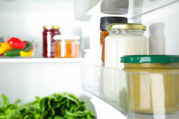 Bottles with different tasty sauces and products in fridge, closeup