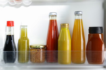 Bottles with different tasty sauces in fridge, closeup