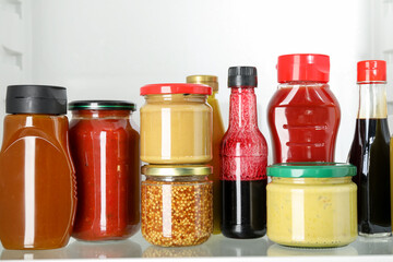 Bottles with different tasty sauces in fridge, closeup